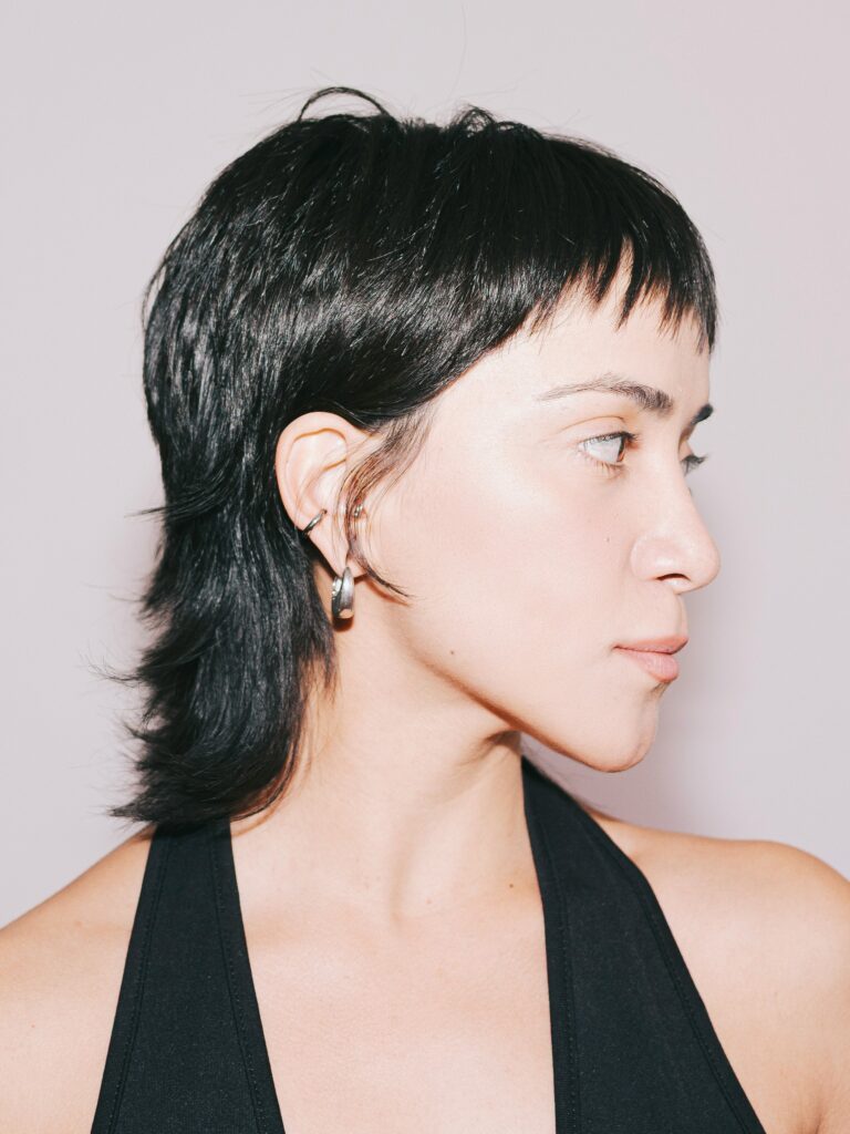 [ALT_TEXT: A young woman with a sleek mullet haircut wearing a black halterneck top.]