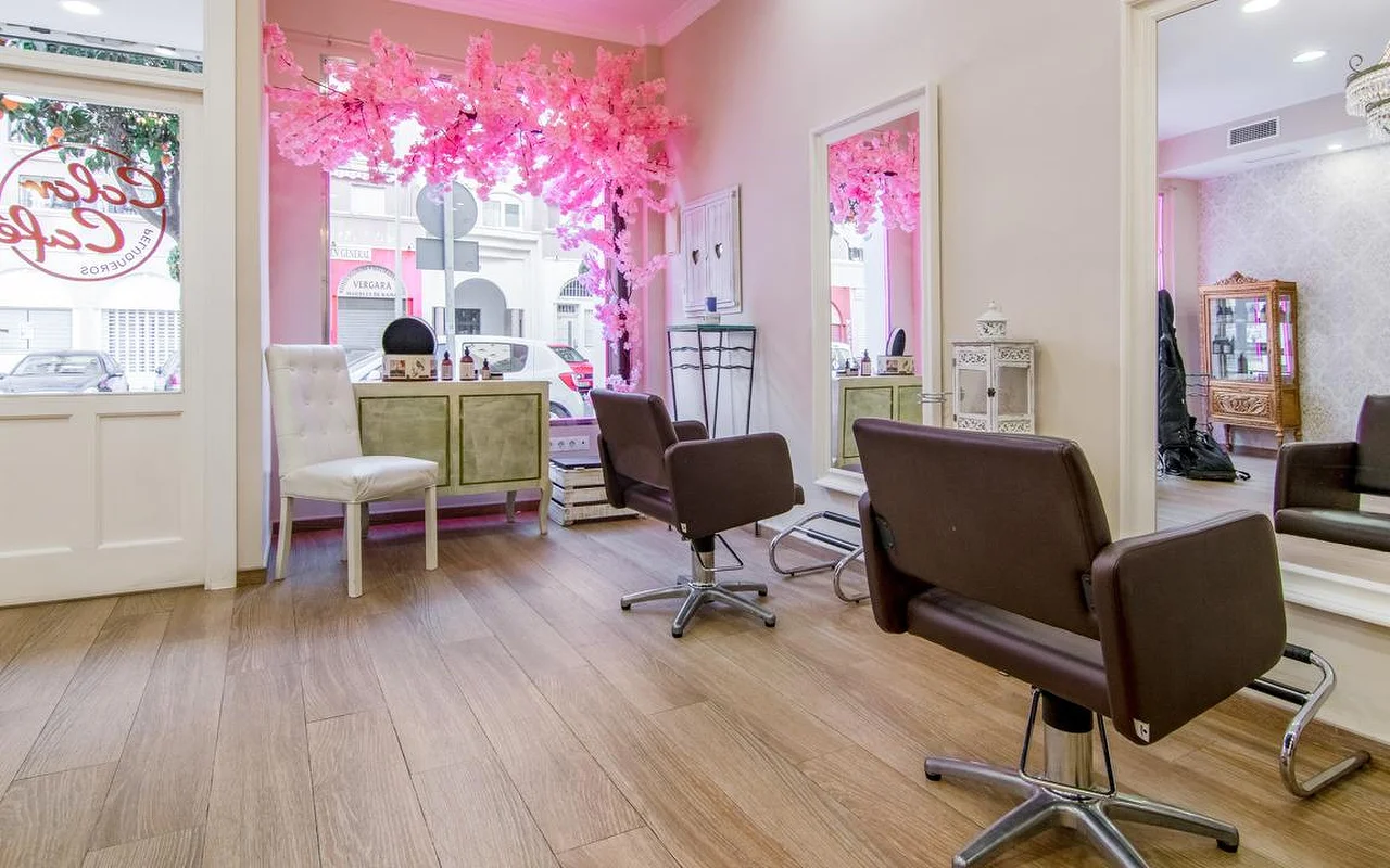 Το εσωτερικό της Color Café Peluqueros στη Torremolinos, ένα κομμωτήριο με ροζ τοίχους, καφέ καρέκλες styling, μεγάλους καθρέφτες και μια ροζ διακόσμηση ανθισμένης κερασιάς στη βιτρίνα.