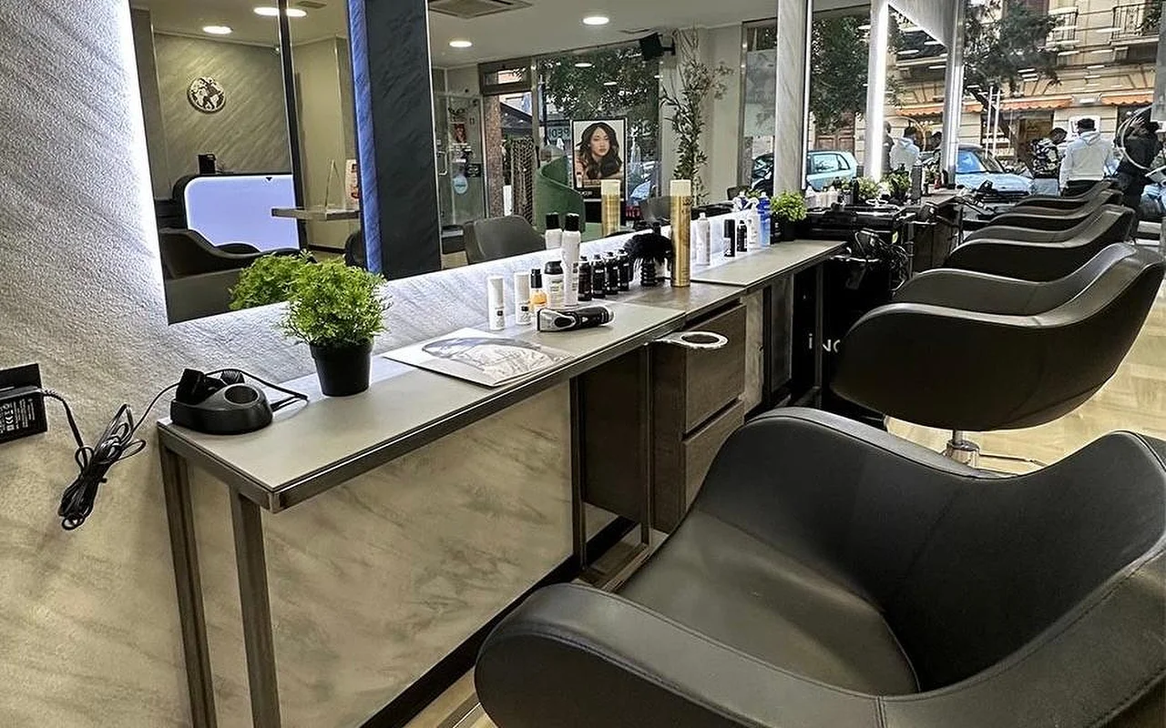 Η ζώνη χτενίσματος του Equipe Beauty, με μια σειρά από μαύρες καρέκλες κατά μήκος ενός πάγκου με όψη μαρμάρου, έναν μεγάλο φωτιζόμενο καθρέφτη, προϊόντα styling και μια γλάστρα πάνω στον πάγκο, και παράθυρα από το δάπεδο ως το ταβάνι που βλέπουν στον δρόμο.