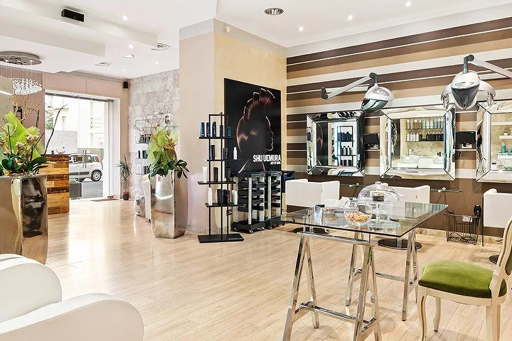Κομψές θέσεις styling στο σαλόνι Hair Queen στο Cagliari με τοίχους σε ρίγες κρεμ και καφέ και ψηλές ασημί γλάστρες.