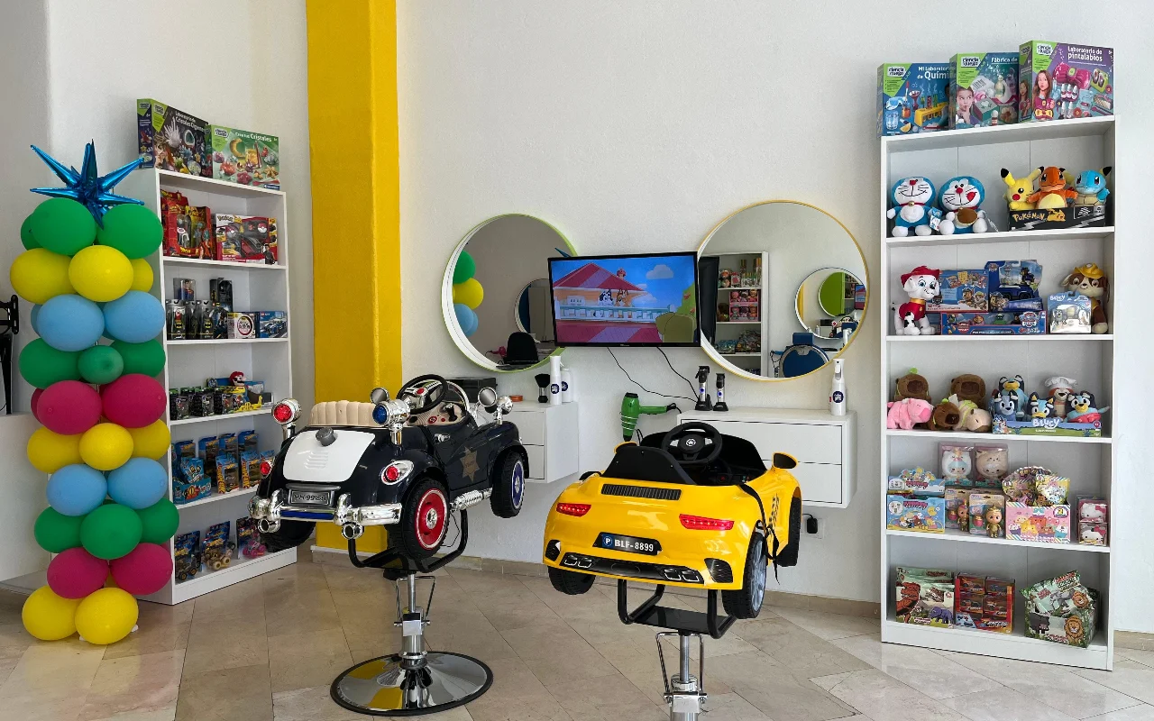 Η παιδική γωνιά της Peluplay στη Benalmádena, όπου οι καρέκλες styling έχουν σχήμα αυτοκινητάκια, με ράφια γεμάτα ήρωες κινουμένων σχεδίων, στρογγυλούς καθρέφτες και μια κολόνα από μπαλόνια.