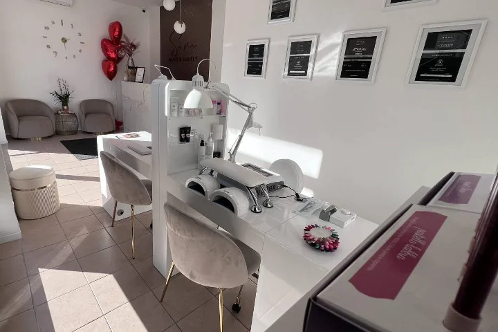Λευκό σαλόνι νυχιών Sara Nails&Beauty στο Tortolì με γκρι βελούδινες καρέκλες και πλαισιωμένα πιστοποιητικά στον τοίχο.